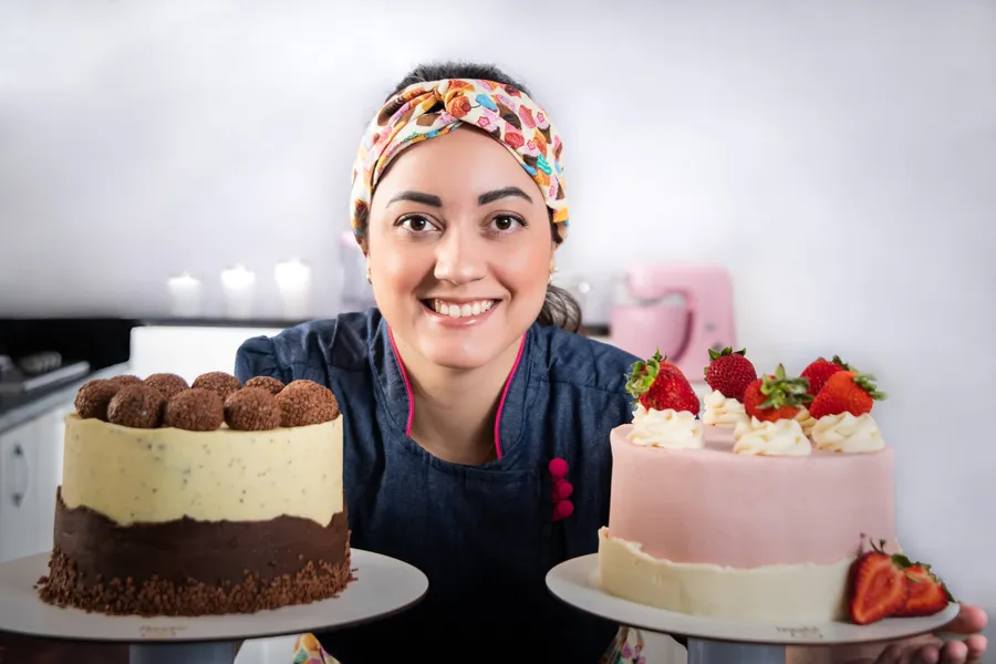 Geórgia, confeiteira da DoceGê, com dois bolos artesanais